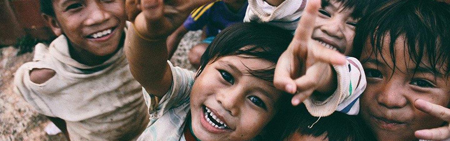 A group of smiling children making peace signs towards the camera.